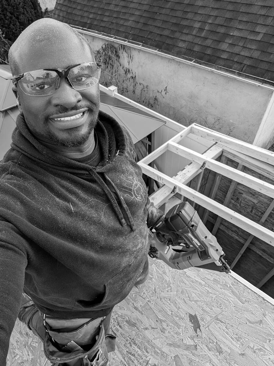Gerald in safety glasses, smiling, holding a nail gun on the roof deck of a shed he is building
